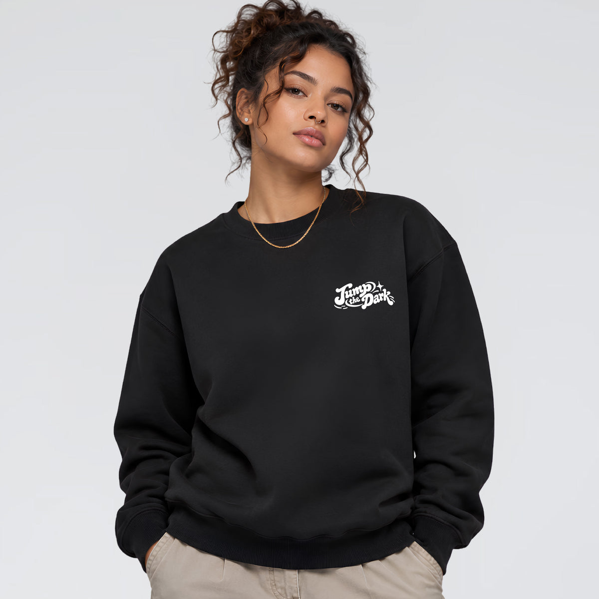 Woman wearing Keep Rolling black crewneck with small white Jump the Dark chest logo