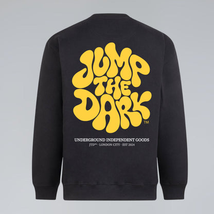 A flat lay image of a black crewneck sweatshirt shown from the back, featuring a large yellow retro-style graphic that reads JUMP THE DARK.