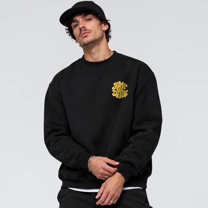 A man wearing a black crewneck sweatshirt with a yellow graphic logo on the left chest.